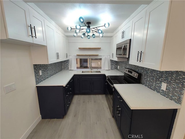 kitchen with white cabinets, appliances with stainless steel finishes, dark cabinets, light countertops, and a sink