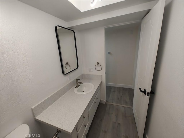 bathroom featuring toilet, wood finished floors, vanity, and baseboards