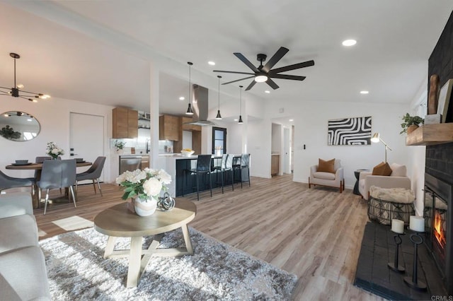 living room with light wood finished floors, a glass covered fireplace, lofted ceiling, ceiling fan, and recessed lighting