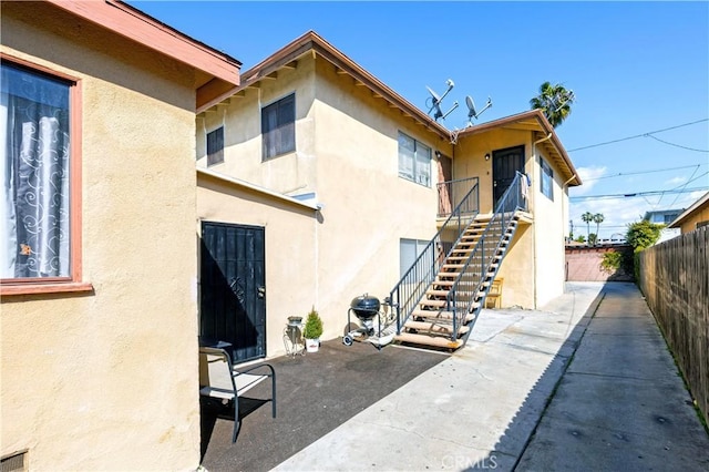 exterior space featuring stucco siding, fence, stairway, and a patio