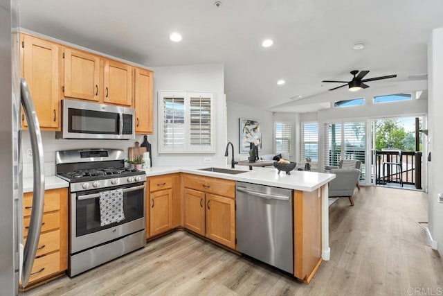 kitchen with stainless steel appliances, light countertops, open floor plan, a sink, and a peninsula