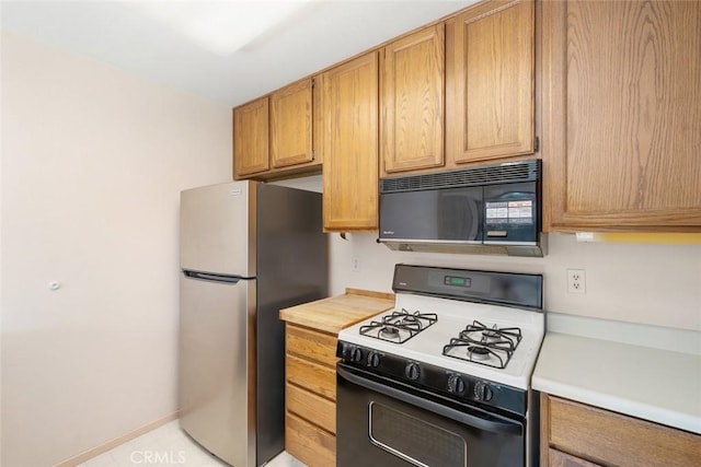 kitchen featuring black microwave, light countertops, freestanding refrigerator, and range with gas stovetop