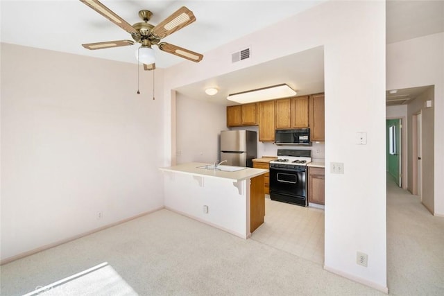 kitchen with brown cabinetry, freestanding refrigerator, white gas range, light countertops, and black microwave