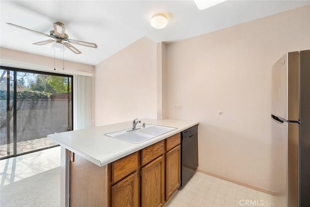 kitchen featuring brown cabinetry, freestanding refrigerator, a sink, dishwasher, and a peninsula