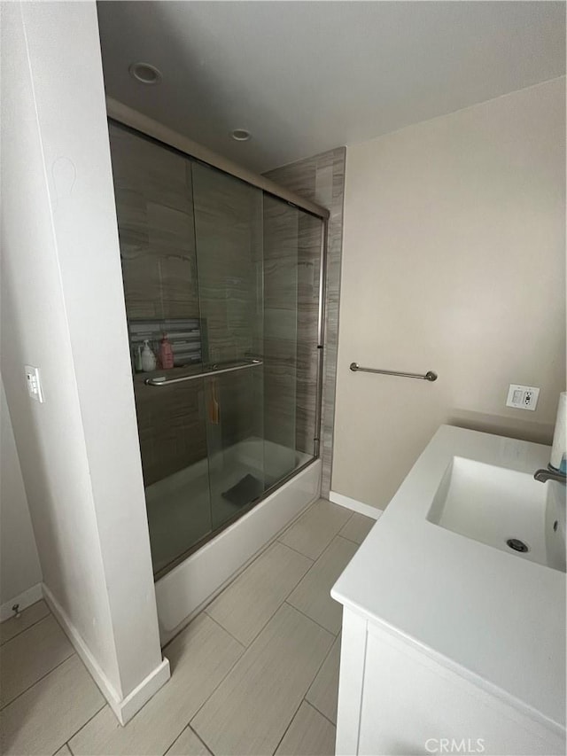 full bath with baseboards, bath / shower combo with glass door, and vanity