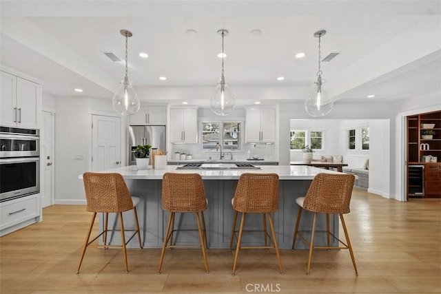 kitchen with a spacious island, light countertops, appliances with stainless steel finishes, white cabinetry, and beverage cooler