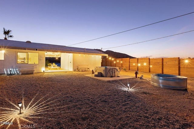 back of house at dusk with a hot tub, a fenced backyard, and a patio