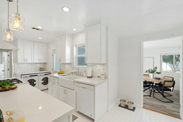 kitchen with washing machine and clothes dryer, light countertops, backsplash, white cabinetry, and white appliances