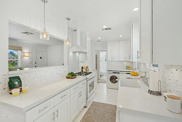 kitchen featuring white cabinets, light countertops, wall chimney range hood, white gas range oven, and washer / clothes dryer