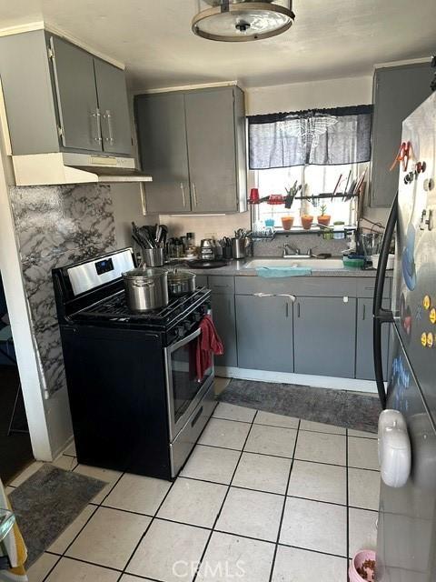 201 W Raymond St, Compton, CA 90220 - kitchen with stainless steel gas range oven, under cabinet range hood, freestanding refrigerator, gray cabinetry, and light tile patterned floors