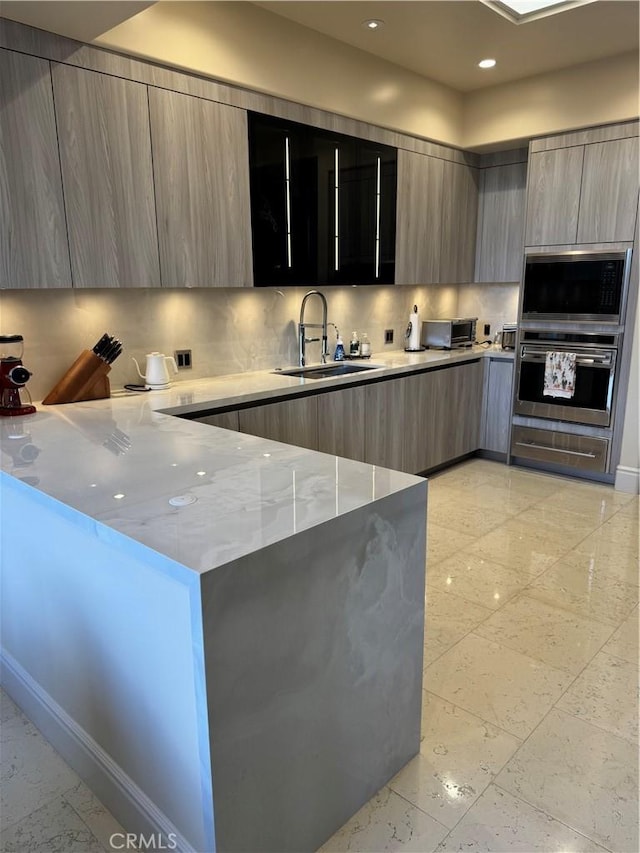 kitchen with light stone countertops, a sink, decorative backsplash, and modern cabinets