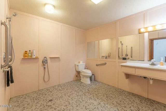 bathroom featuring a shower, a decorative wall, a sink, and toilet