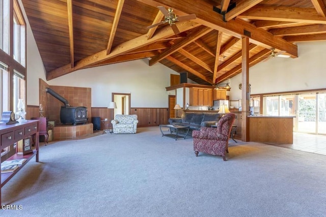 carpeted living area featuring beamed ceiling, a wood stove, wainscoting, and wood ceiling
