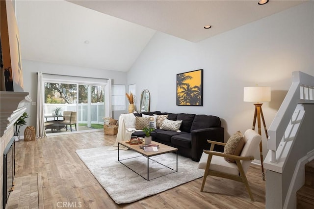 living room featuring stairway, wood finished floors, a fireplace, high vaulted ceiling, and recessed lighting