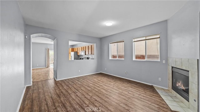 unfurnished living room featuring light wood finished floors, baseboards, a fireplace, and arched walkways