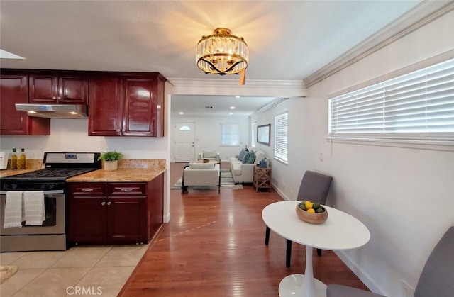 kitchen with reddish brown cabinets, under cabinet range hood, crown molding, and stainless steel gas stove
