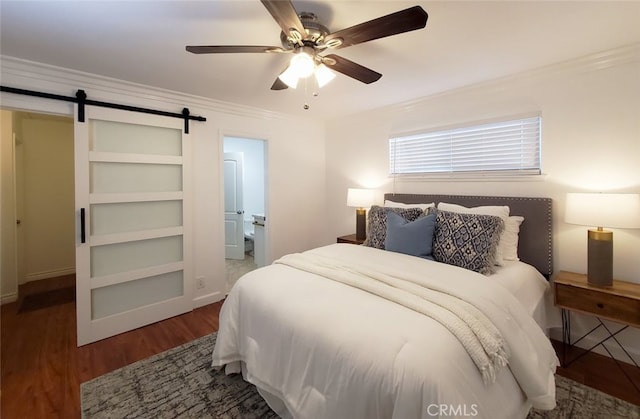 bedroom featuring a barn door, wood finished floors, ceiling fan, crown molding, and ensuite bath