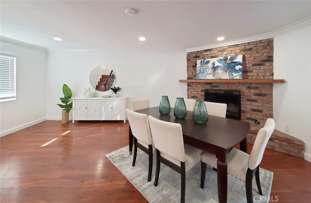 dining room featuring crown molding, wood finished floors, baseboards, a brick fireplace, and recessed lighting