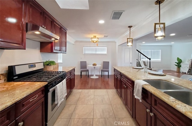 kitchen with under cabinet range hood, stainless steel gas range, pendant lighting, ornamental molding, and visible vents