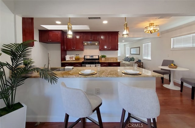 kitchen featuring a sink, visible vents, gas range, reddish brown cabinets, and under cabinet range hood