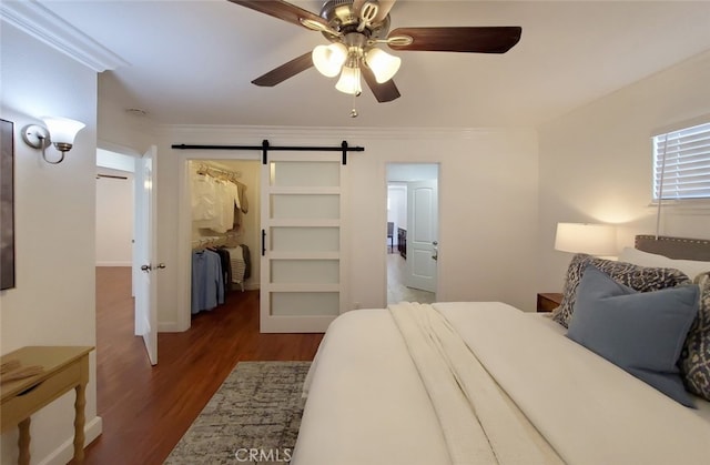 bedroom featuring a barn door, a spacious closet, wood finished floors, ceiling fan, and ornamental molding