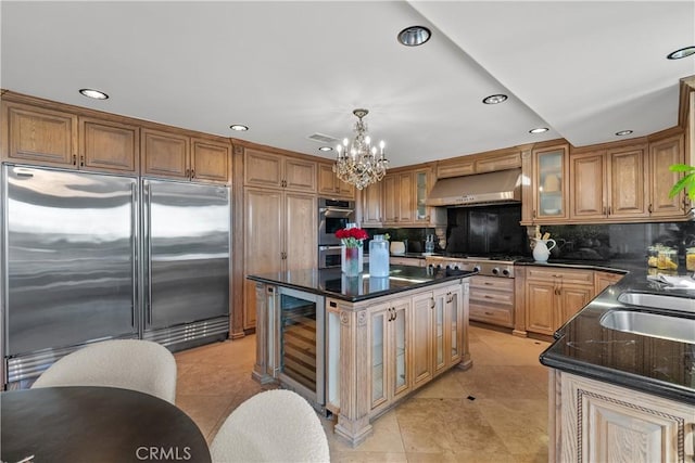 kitchen with wall chimney exhaust hood, wine cooler, glass insert cabinets, appliances with stainless steel finishes, and a center island