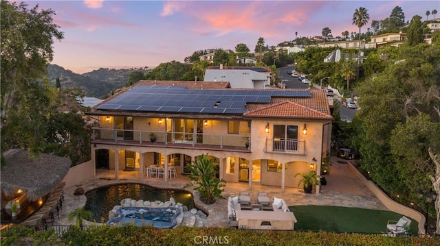 back of property at dusk featuring a patio, a balcony, an outdoor hangout area, fence, and an outdoor pool