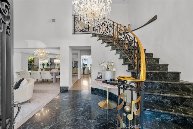 foyer entrance with marble finish floor, visible vents, a towering ceiling, an inviting chandelier, and stairs