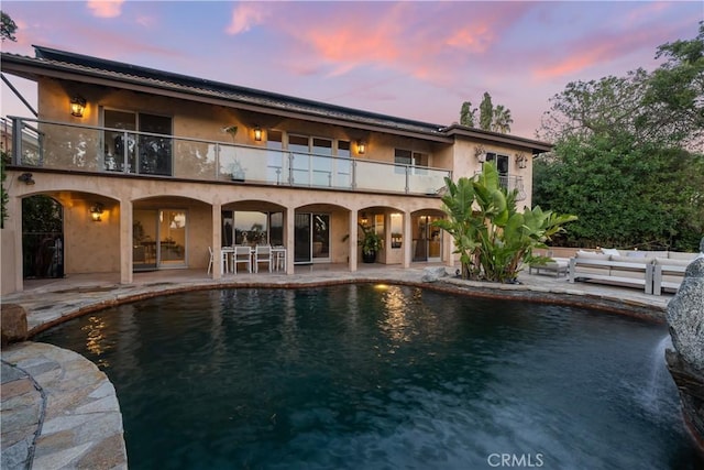 rear view of house featuring stucco siding, an outdoor pool, a balcony, and a patio