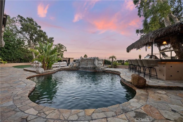 pool at dusk with a patio area, an outdoor pool, and outdoor dry bar