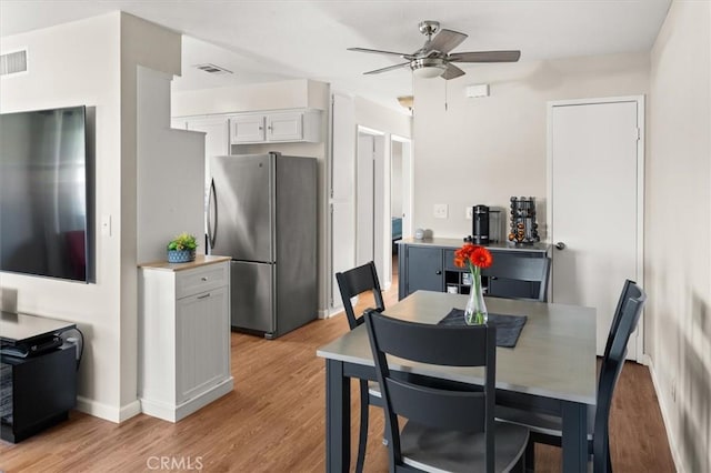 dining room featuring light wood finished floors, baseboards, visible vents, and a ceiling fan