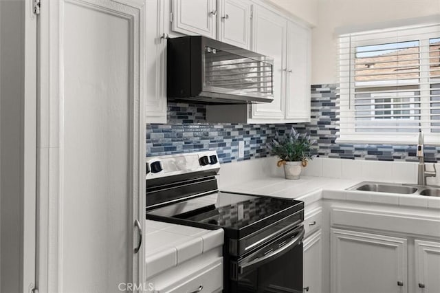 kitchen featuring stainless steel electric stove, tile counters, white cabinetry, a sink, and black microwave