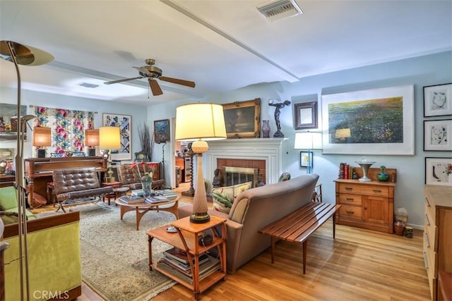 living room featuring light wood-type flooring, a fireplace, visible vents, and a ceiling fan