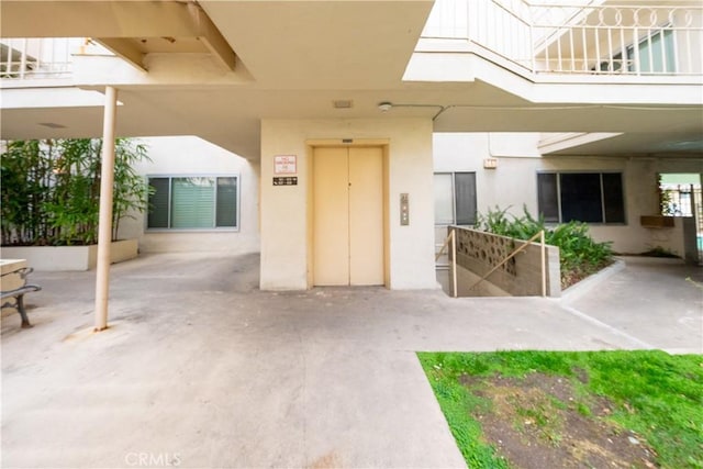 property entrance featuring a balcony, elevator, a patio area, and stucco siding