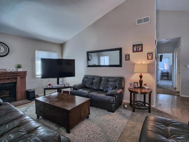 living area featuring high vaulted ceiling, a brick fireplace, visible vents, and baseboards