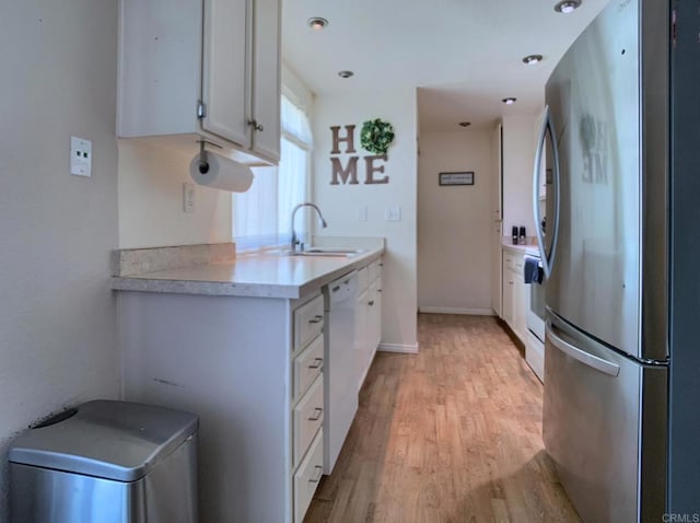 kitchen featuring a sink, light countertops, light wood-type flooring, freestanding refrigerator, and dishwasher