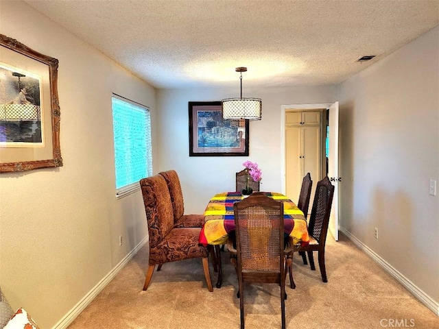 dining room featuring baseboards, light colored carpet, visible vents, and a textured ceiling