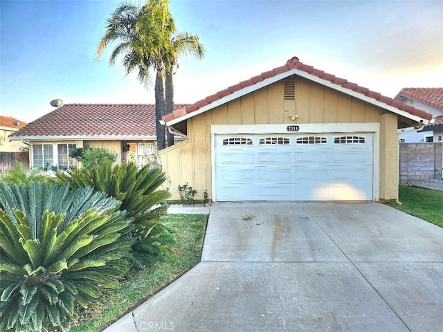 view of front facade with a tile roof, driveway, an attached garage, and fence