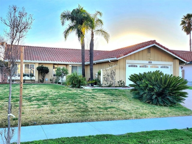 view of front of home featuring a tiled roof, a yard, and an attached garage