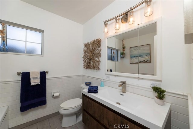 bathroom with toilet, vanity, tile walls, and wainscoting