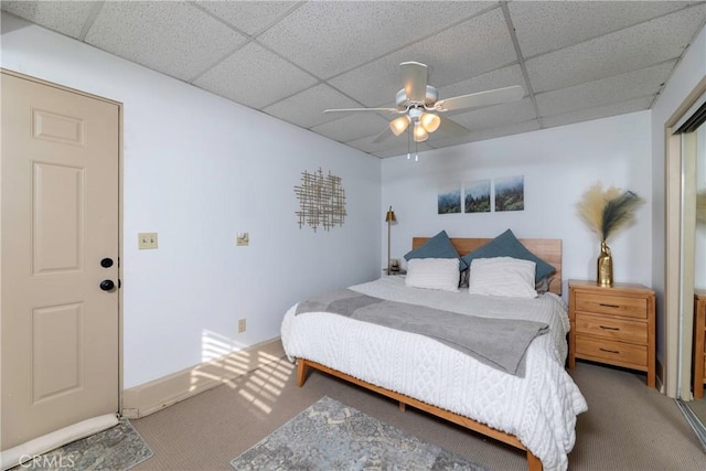 carpeted bedroom featuring ceiling fan, baseboards, and a drop ceiling