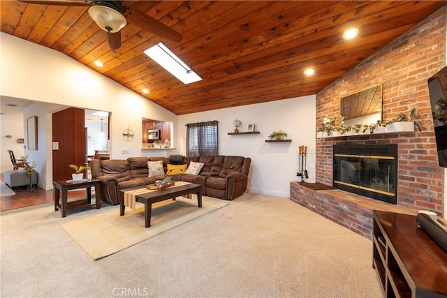 living room featuring ceiling fan, vaulted ceiling with skylight, carpet floors, a fireplace, and wood ceiling