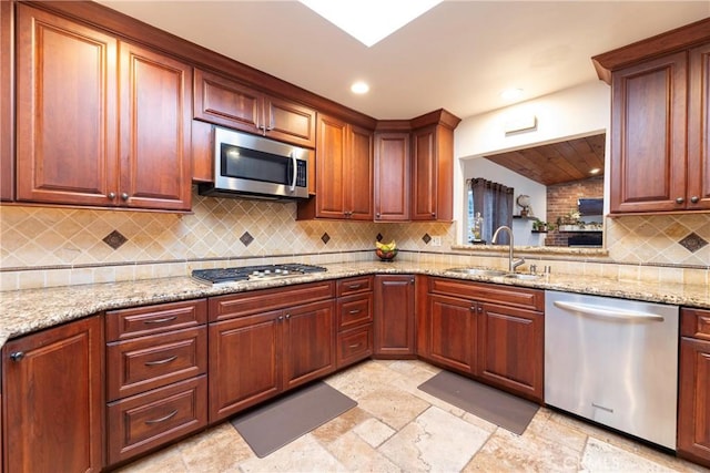 kitchen with appliances with stainless steel finishes, backsplash, a sink, and light stone counters