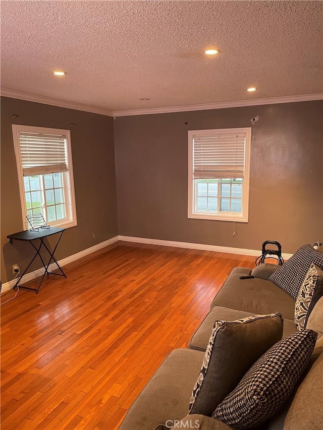 living area featuring wood-type flooring, a healthy amount of sunlight, crown molding, and baseboards