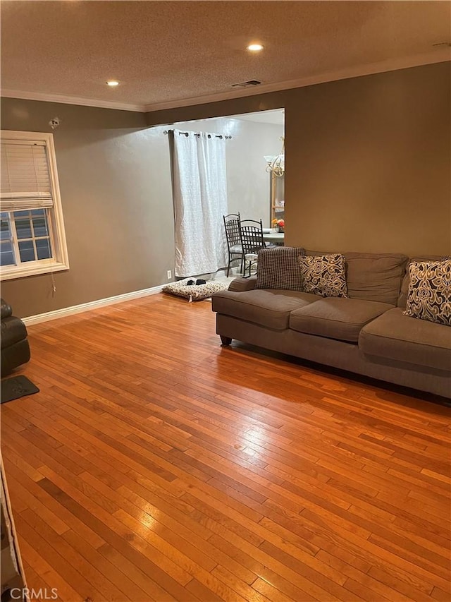 living area with visible vents, ornamental molding, a textured ceiling, light wood-type flooring, and baseboards