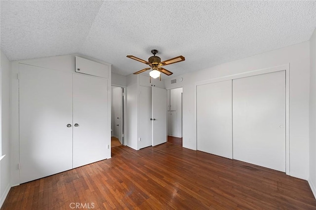 unfurnished bedroom with visible vents, dark wood finished floors, ceiling fan, a textured ceiling, and two closets