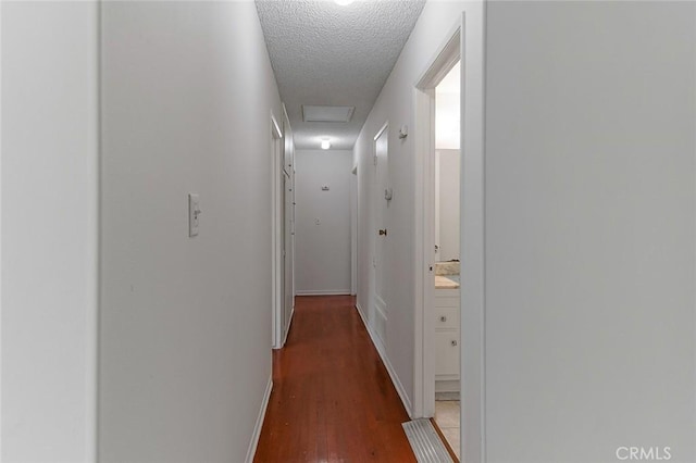 hall featuring dark wood-style floors, attic access, baseboards, and a textured ceiling