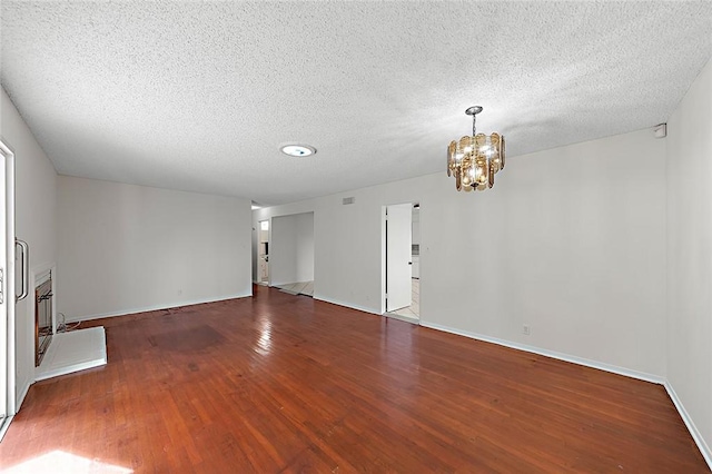 unfurnished living room with a textured ceiling, dark wood-style flooring, baseboards, and an inviting chandelier