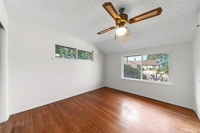 spare room featuring a textured ceiling, baseboards, wood finished floors, and lofted ceiling