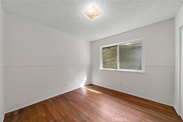 unfurnished room with a textured ceiling and wood finished floors